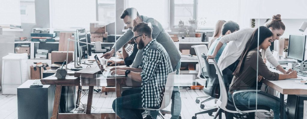 Discussing business issues. Group of young business people sitting at the office desk and discussing something while working together behind the glass wall in creative office